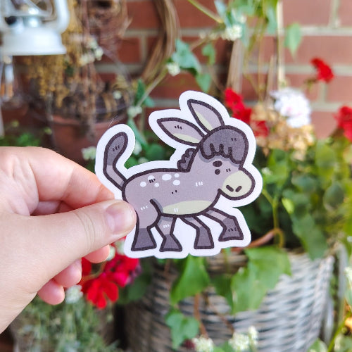 Kuvassa on aasitarra. Aasi on harmaa. Aasilla on hieman tuima ilme ja se polkee jaloillaan maata. Perus aasi.