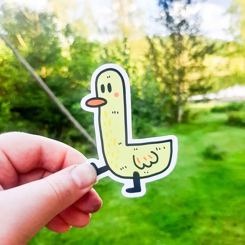 Kuvassa on keltainen ankkatarra. Ankalla on pitkä kaula, oranssi nokka ja hieman mietteliäs ilme. Ankan jalat ovat mustat ja se näyttää vaappuvan hauskasti eteenpäin.