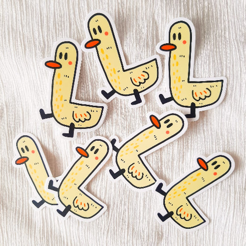 Kuvassa on keltainen ankkatarra. Ankalla on pitkä kaula, oranssi nokka ja hieman mietteliäs ilme. Ankan jalat ovat mustat ja se näyttää vaappuvan hauskasti eteenpäin.