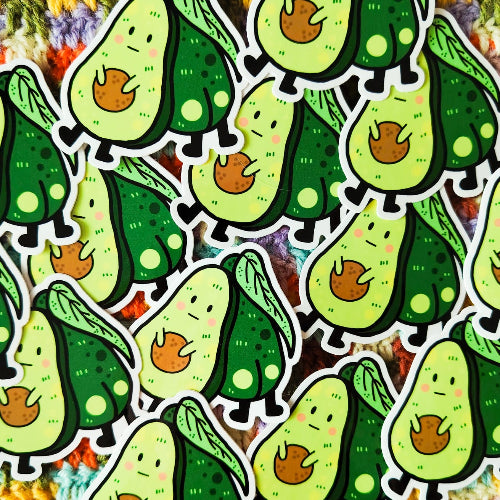 Kuvassa on tarra, jossa on kaksi avokadoa. Toinen on myrtsin näköinen avokado ja toinen heistä piilottelee ensimmäisen avokadon takana, niin että hänen pyllyvako näkyy.