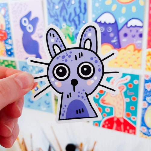 Kuvassa on tarra, joka on violetinsininen kissa. Kissalla on komeat pitkät viikset ja isot silmät ja korvat.