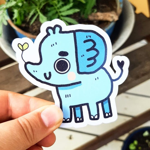 Kuvassa on sininen norsutarra. Norsulla on iloinen ilme ja sen kärsästä tulee kasvi ulos.