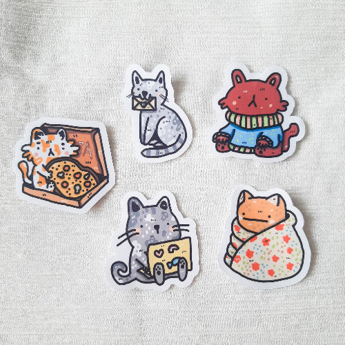 Kuvassa on viisi erilaista kissatarraa valkoisella taustalla. Kissat ovat kaikki hieman erilaisia.