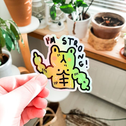 Kuvassa oleva tarra on vihreä sammakko. Sammakolla on valtavat vatsalihakset ja lihaksikkaat kädet, ja hieman apea ilme. Sillä on myös oikein pinkit posket. Tarran päällä lukee "I'm strong!" eli "olen vahva". Tarra on holograafinen, ja se heijastaa sateenkaaren väreissä.