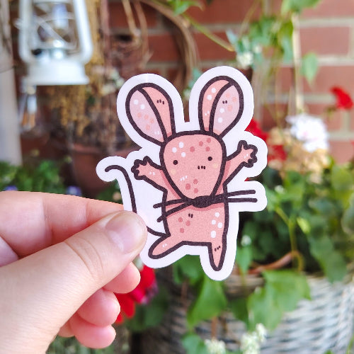 Kuvassa on vaaleanpunainen hiiritarra. Hiirellä on pitkä häntä ja sen kädet ovat ylöspäin, aivan kuin valmiina halaukseen.