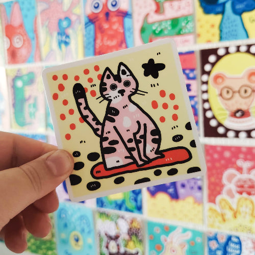 Kuvassa on neliön muotoinen kissatarra. Kissa on vaaleanpunainen ja siinä on mustia ja valkoisia laikkuja.