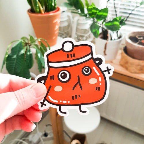 Kuvassa oleva vedenkestävä tarra on punainen emalikattila, jolla on hauska ilme. Sillä on suuret silmät ja punaiset posket.