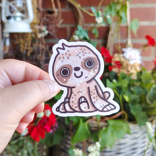 Kuvassa on hauska laiskiaistarra. Laiskiainen istuu ja hymyilee suurella suullaan.