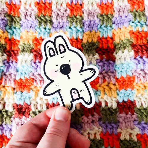 Kuvassa oleva hauska vedenkestävä tarra on vaalean beige pupu. Pupulla on vaaleanpunainen maha ja posket, ja sillä näkyy napa. Pupun kädet ovat kuin valmiina halaukseen.