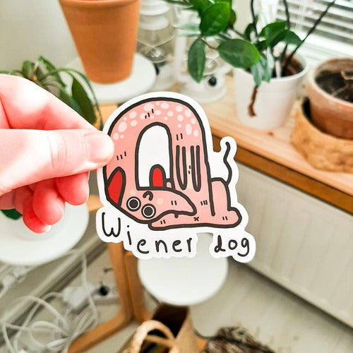 Kuvassa on mutkalla oleva mäyräkoira. Koiralla on niin pitkä selkä, että se kaartuu nätisti itsensä ympäri. Koiralla on hauska ilme ja suuret silmät Kuvassa koiran alla lukee "Wiener dog".