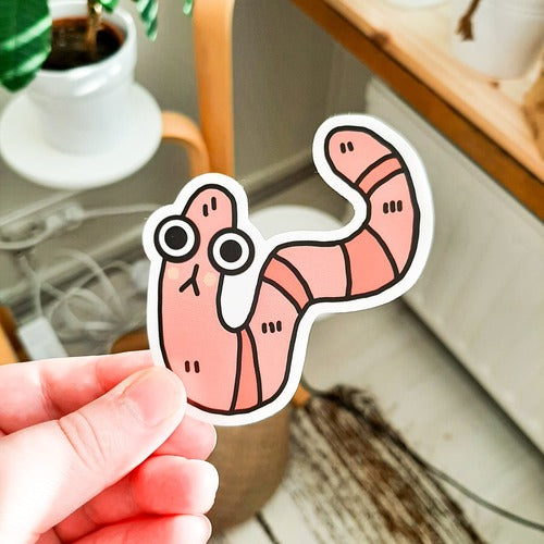 Kuvassa on hauska matotarra. Mato on pinkki ja sillä on suuret silmät.