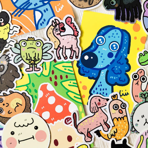 Söpöt ja värikkäät tarrat ja postikortit aseteltuna valkoisen kankaan päälle. Tarrat ovat kooltaan 7,5 cm ja postikortit A6-kokoisia. Tuotteissa seikkailevat iloiset ja hauskat eläinhahmot.