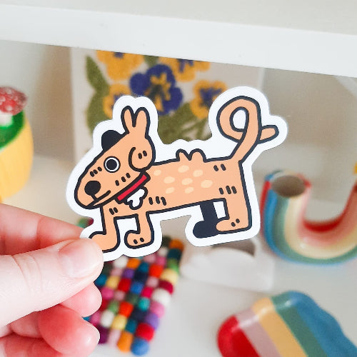 Kuvassa oleva tarra on ruskea koira. Koiran vartalo on hieman mäyräkoiramainen, ja sen pitkä häntä on kippuralla. Koiralla on punainen kaulapanta.