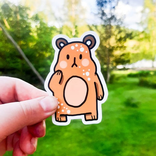 Kuvassa oleva vedenkestävä tarra on ruskea nalle, jolla on pehmoisen näköinen vaaleanpunainen vatsa. Söpöllä nallella on oikein mietteliäs ilme, ja se on nostanut toisen kätensä poskelle. Hauskalla karhulla on lyhyet jalat.