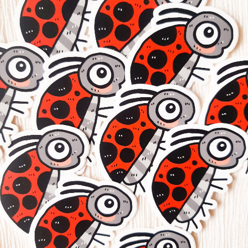 Kuvassa on leppäkerttutarra. Leppäkertulla on kirkkaanpunainen selkä, jossa on erikokoisia mustia pilkkuja. Leppäkertulla on harmaa vartalo ja suuret silmät. Leppäkerttu on pirteän värikäs ja iloisen näköinen.