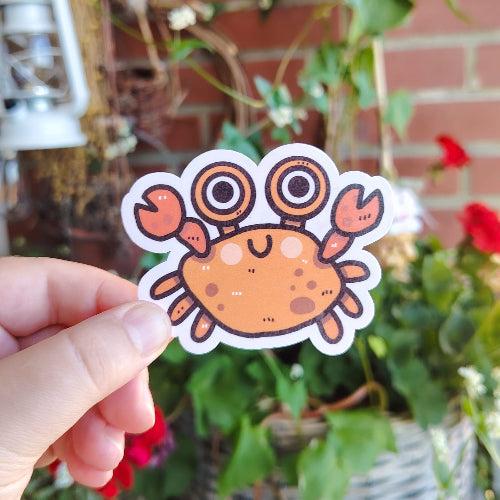 Kuvassa on oranssi rapu. Ravulla on hauskat kädet, isot silmät ja iloinen hymy.