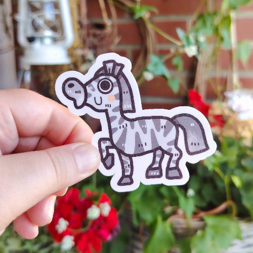 Kuvassa on harmaaraidallinen seepra, joka hymyilee. Sillä on isot silmät, pinkit posket ja iso turpa.