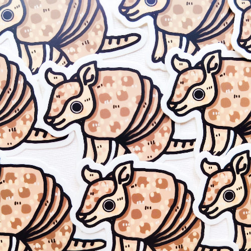 Kuvassa on vaaleanruskea vyötiäinen, joka istuu. Vyötiäisellä on hymy huulilla ja sillä on suuret korvat ja suuret silmät.