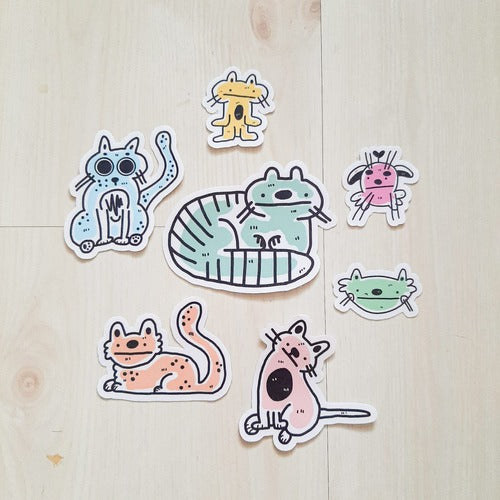 Kuvassa on värikkäitä kissatarroja. Jokainen tarra on erivärinen, ja niiden pohja on valkoinen. Tarrat ovat yksinkertaistettuja ja hauskoja.