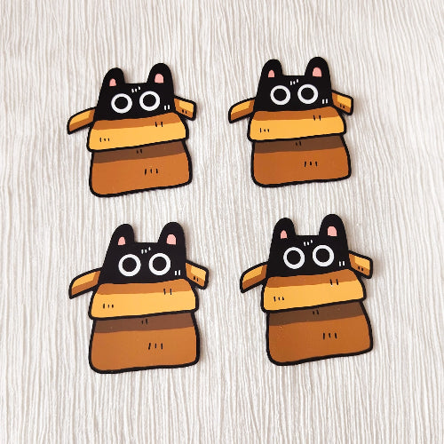 Monta samanlaista magneettia, jossa on kissa. Kuvan kissa on ruskeassa pahvilaatikossa ja katsoo sieltä keskittyneenä suurilla silmillään.