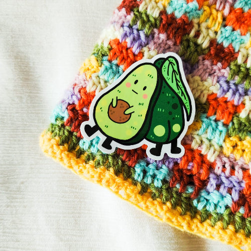 Kuvassa on tarra, jossa on kaksi avokadoa. Toinen on myrtsin näköinen avokado ja toinen heistä piilottelee ensimmäisen avokadon takana, niin että hänen pyllyvako näkyy.