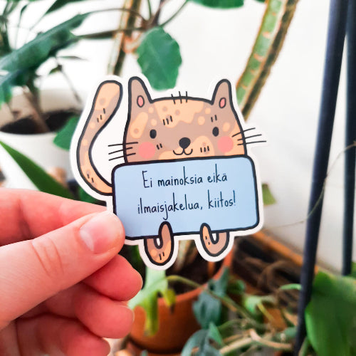 Kuvassa on ulko-oveen tai postilaatikkoon laitettava tarra, jossa lukee "Ei mainoksia eikä ilmaisjakelua, kiitos". Tarran aiheena on kissa.