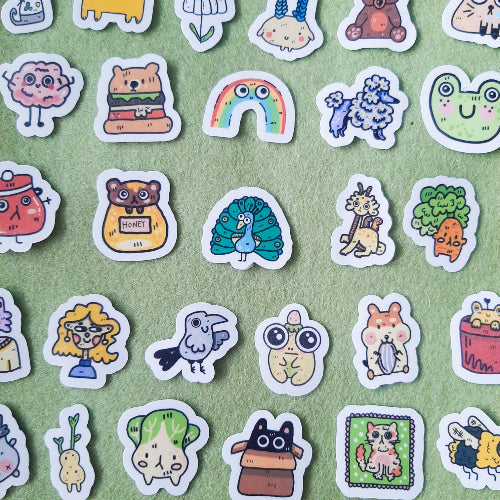 Kuvassa on paljon pieniä, hauskoja tarroja vihreän pohjan päällä. Tarrat ovat pääasiassa eläimiä.
